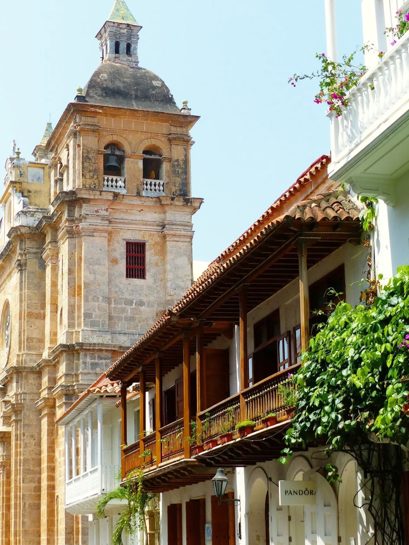 La torre de una iglesia colonial y un balcón de madera con flores, en el centro de Cartagena