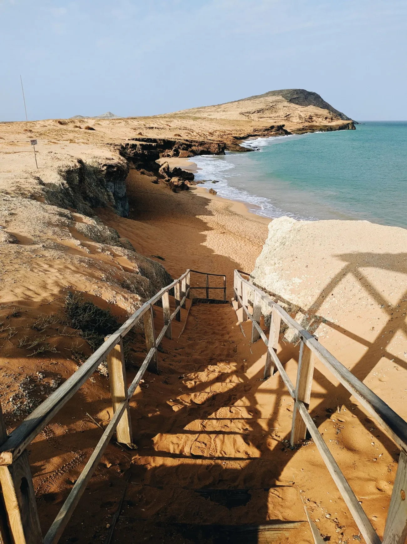Unas escaleras de madera bajando a una playa de arena rojiza, en La Guajira