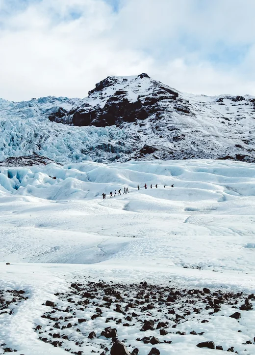 Una fila de personas cruzando a pie el glaciar Sólheimajökull, en Islandia, entre hielo azul y montañas oscuras